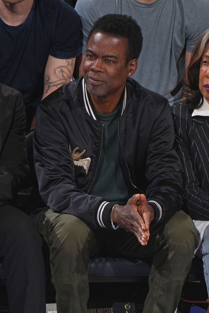 A person in a casual outfit sits in a crowd, hands clasped, appearing attentive