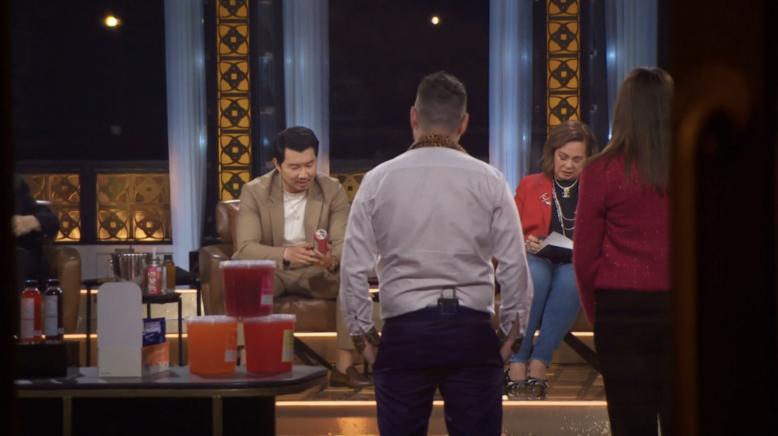 A panel discussion on a stage with four people seated, talking, and some beverages on a table. Names are not provided