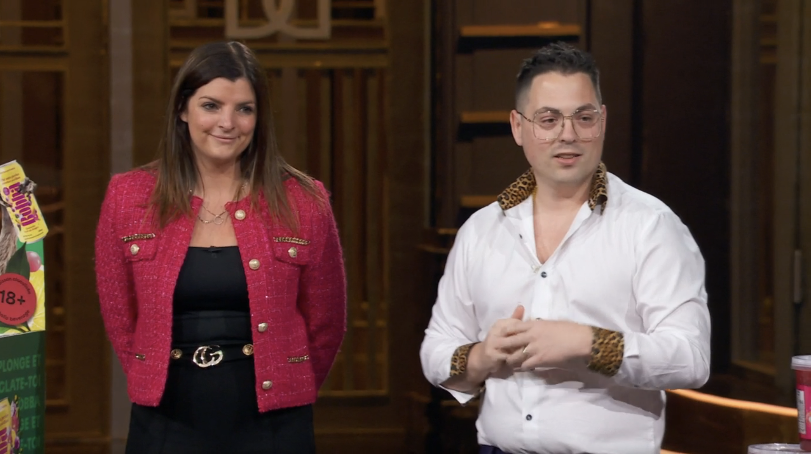 Two people stand together; one wears a red blazer, and the other a white shirt with animal print accents