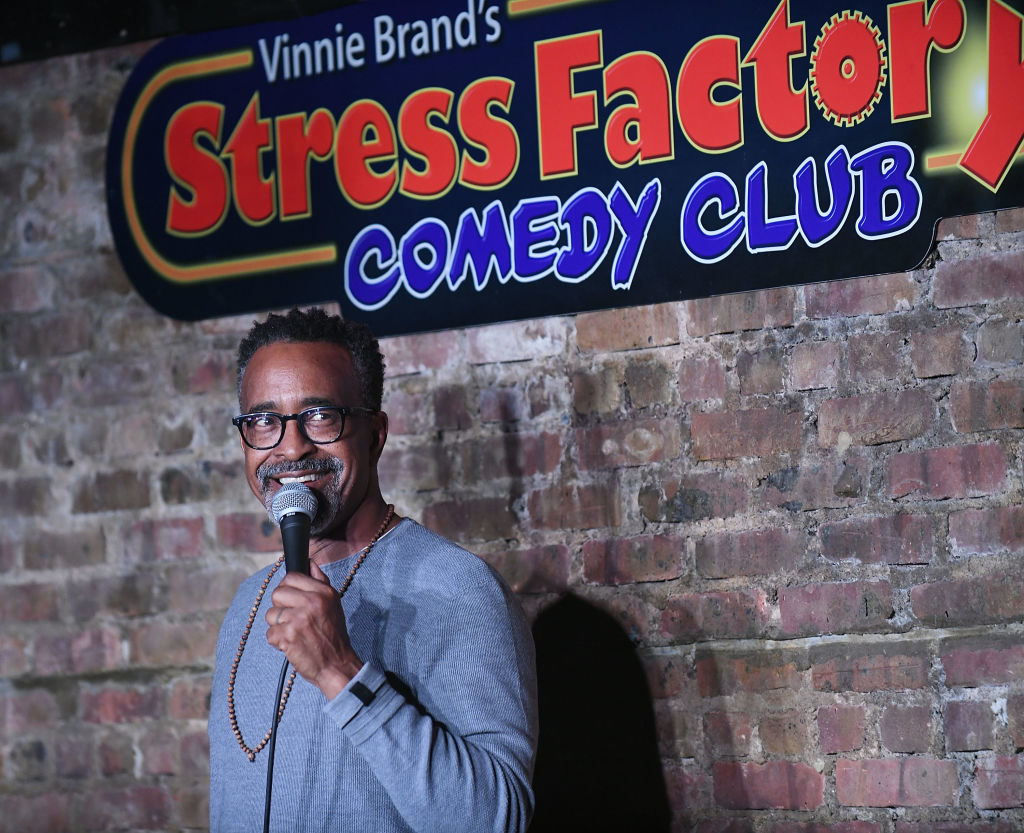 Comedian performing at Vinnie Brand&#x27;s Stress Factory Comedy Club, holding a microphone and smiling at the audience