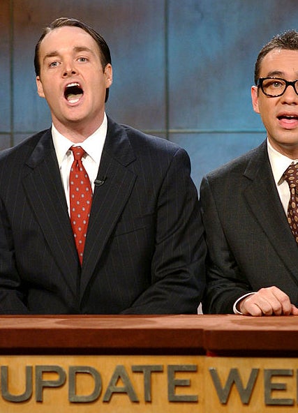 Two men in suits sit behind a &quot;Weekend Update&quot; news desk on a TV set