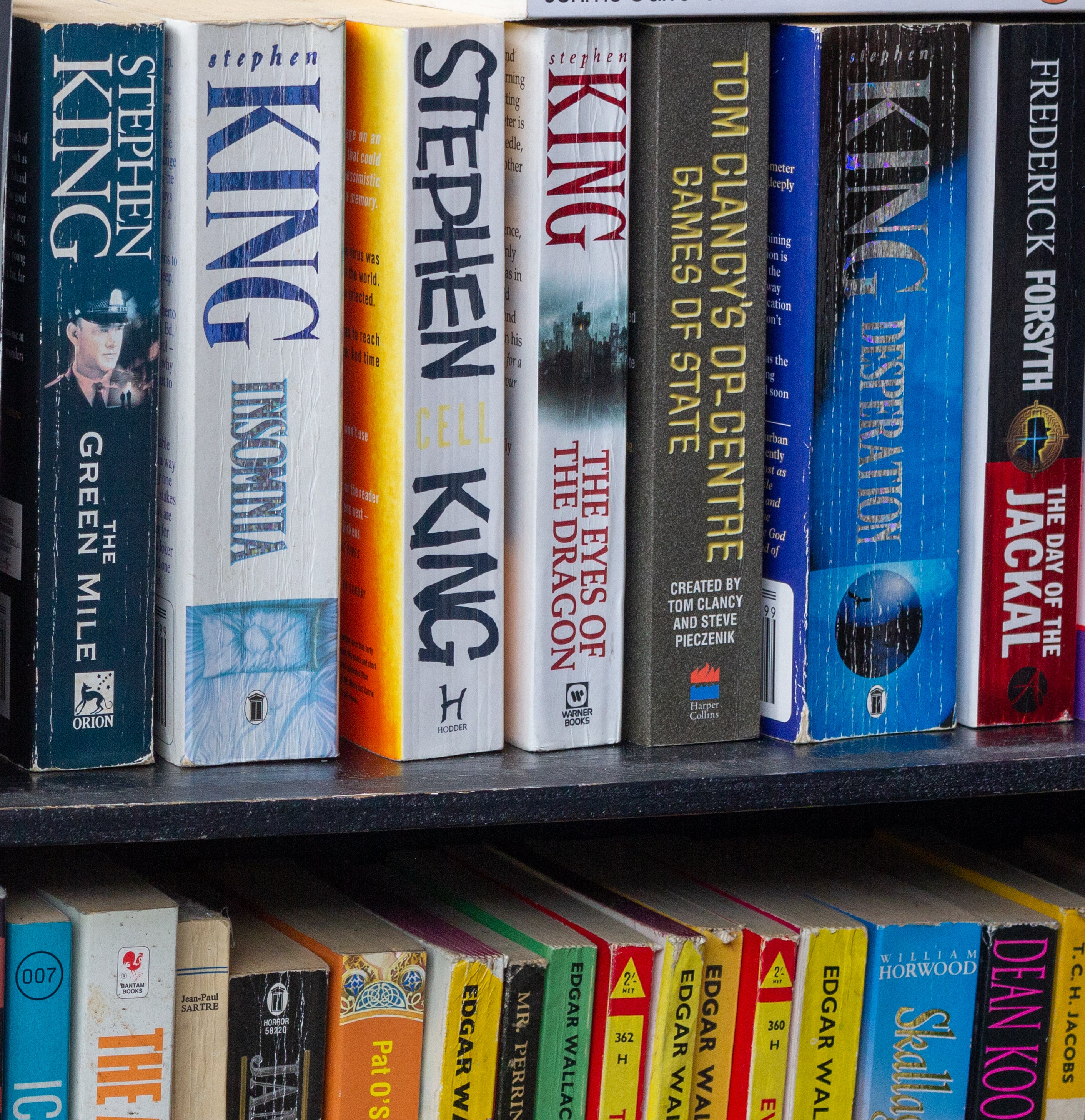 A variety of novels on a bookshelf, including works by Stephen King, John le Carré, and Frederick Forsyth