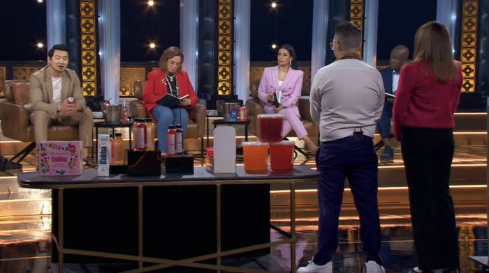 Five people seated and standing in a panel discussion setup with various products displayed on a table