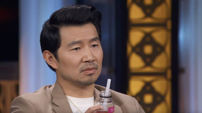Simu Liu sits down holding a bottle of a drink