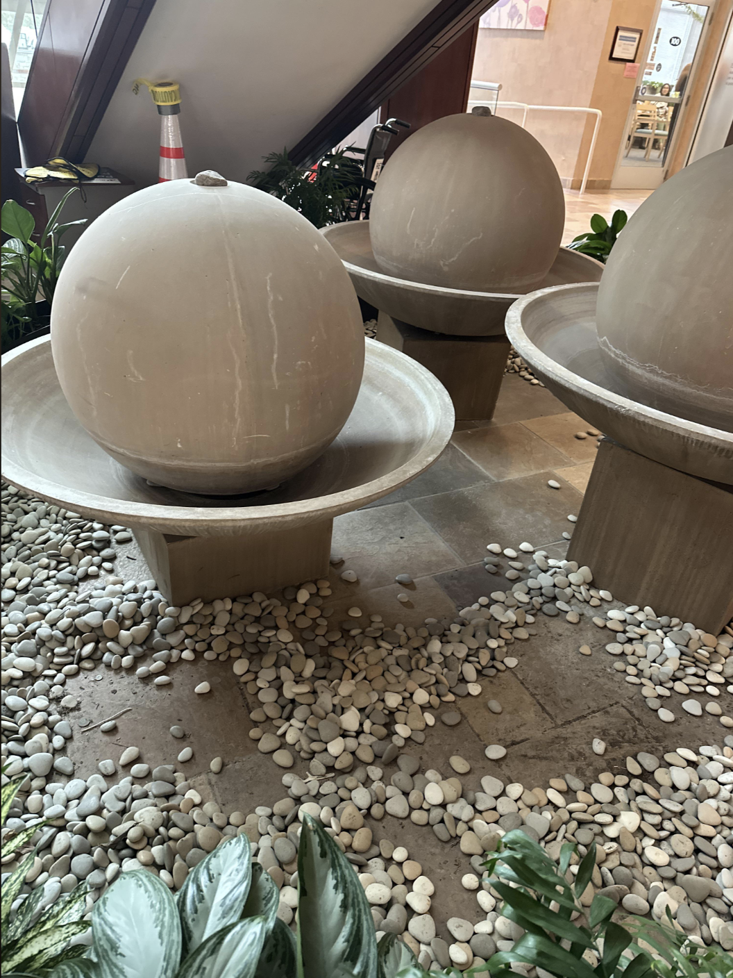 Three large stone spheres sit in circular basins, surrounded by pebbles and plants, inside a building