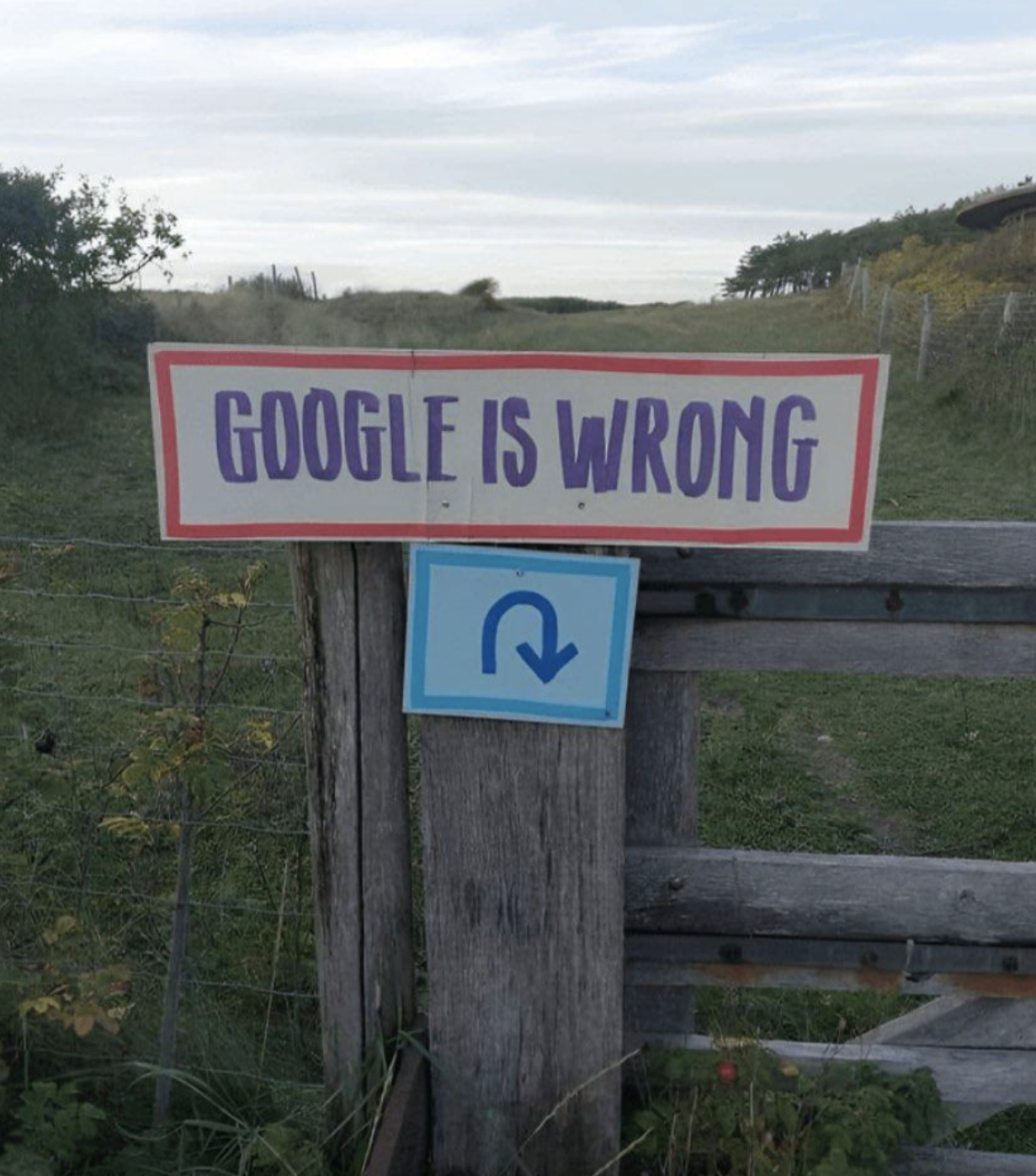 Sign on a wooden gate in a rural setting with the text &quot;Google is wrong&quot; and a U-turn arrow