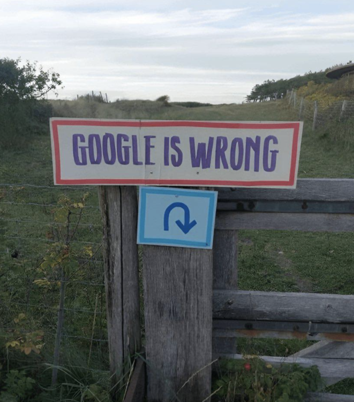 Sign on a wooden gate in a rural setting with the text "Google is wrong" and a U-turn arrow