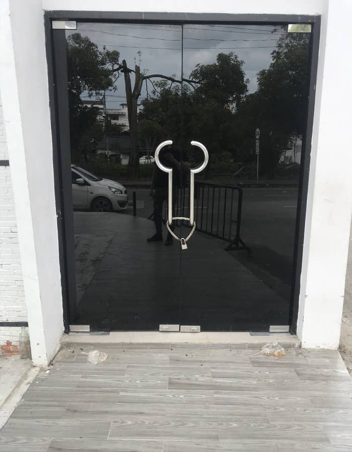 A glass door with a handle shaped like a whimsical outline of a phallic symbol, set against a street view