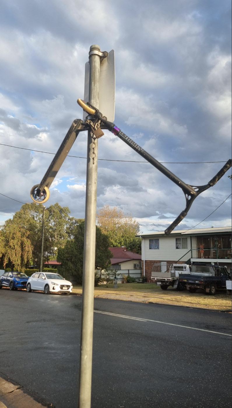 Broken bicycle frame locked to a signpost on a suburban street, with clouds in the sky