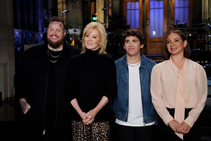 Four people in a group photo, a man in dark clothing, a woman in a black top with leopard print skirt, a young man in a denim jacket, and a woman in a pink blouse