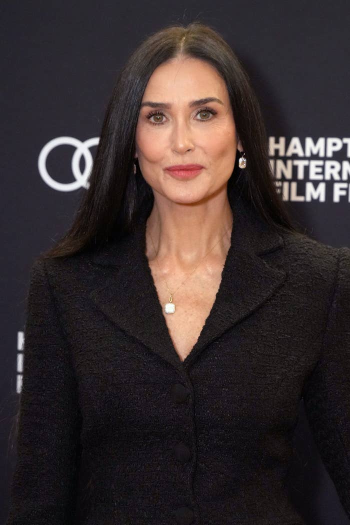 A person with long dark hair is wearing a textured black suit jacket at a film festival event