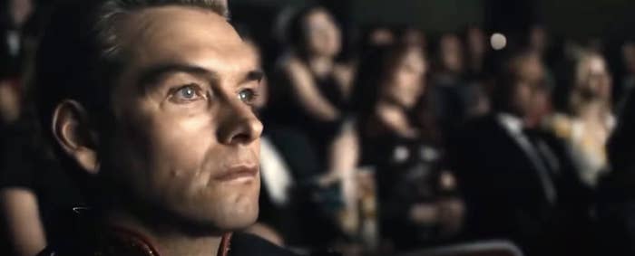 A person in a dimly lit theater looks ahead intently; others are blurred in the background