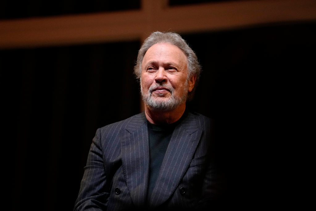 A person in a dark pinstripe suit sits and smiles thoughtfully