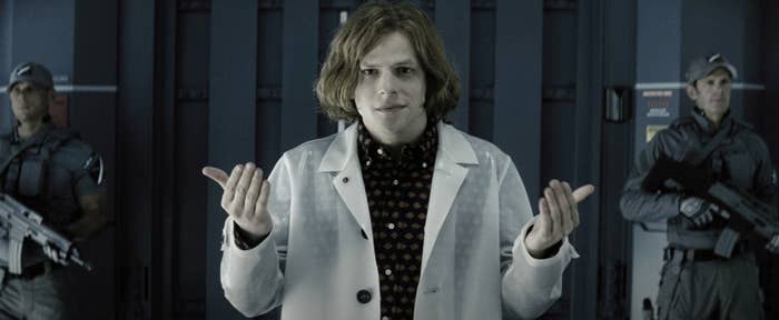 A person in a lab coat stands confidently, flanked by two armed guards. The setting appears to be industrial or high-security