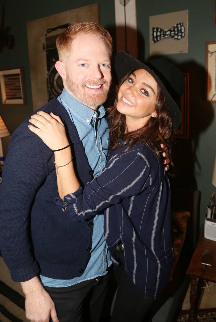 Two people smiling, one wearing a blue cardigan and the other in a black hat and striped shirt
