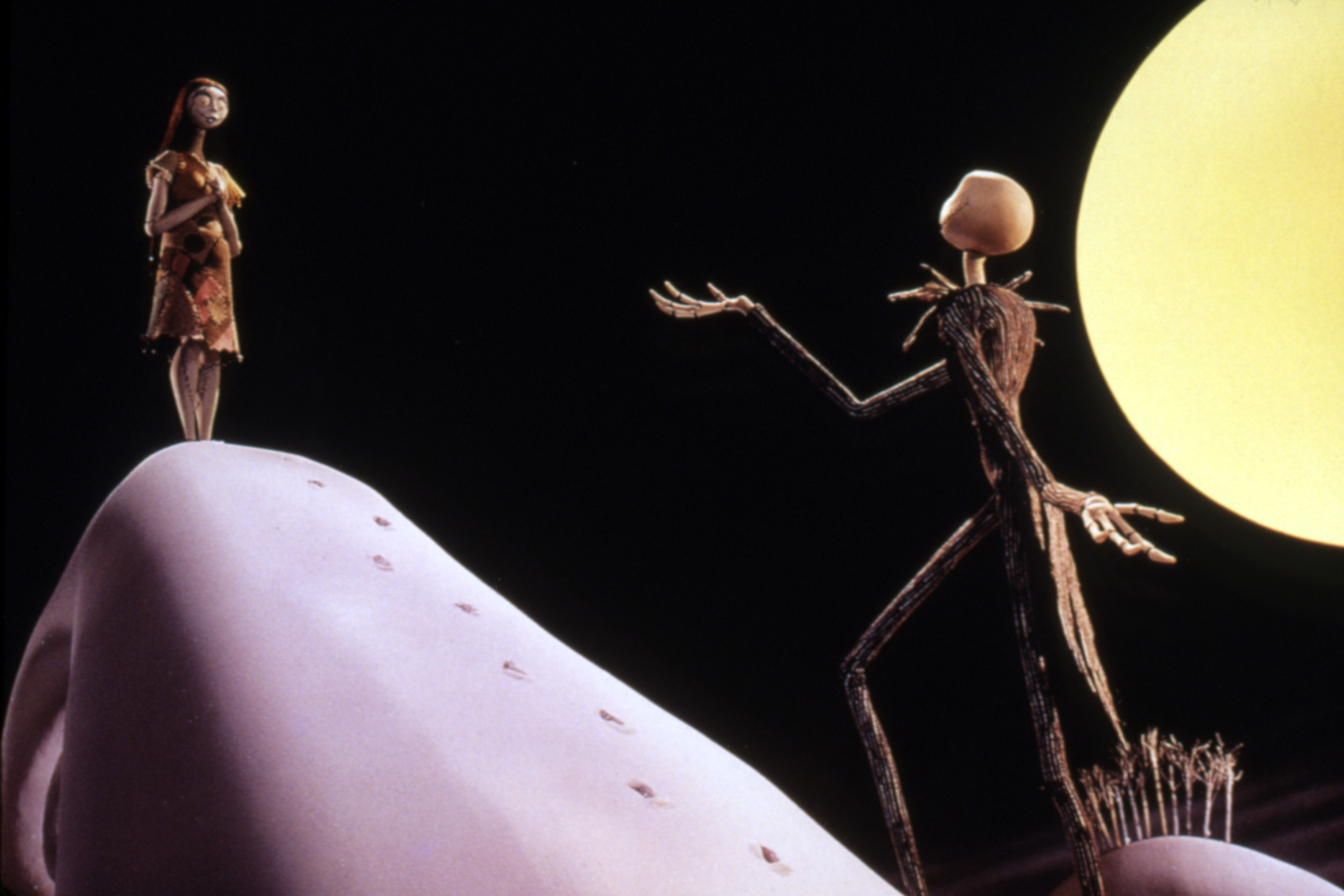 Sally and Jack Skellington from &quot;The Nightmare Before Christmas&quot; stand on a hill under a full moon, facing each other in a dramatic pose