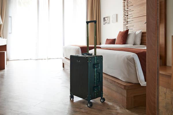 A suitcase stands in a modern hotel room with a neatly made bed and large windows in the background