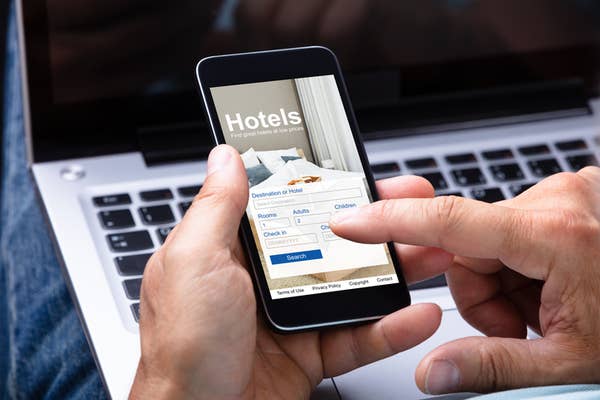 Person holding a smartphone with a hotel booking app open, featuring fields for destination, dates, number of adults, and children