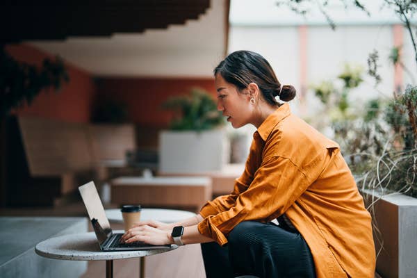I don't know who this is, but a person is sitting at a table, focused on a laptop, with a coffee cup nearby, wearing a button-up shirt