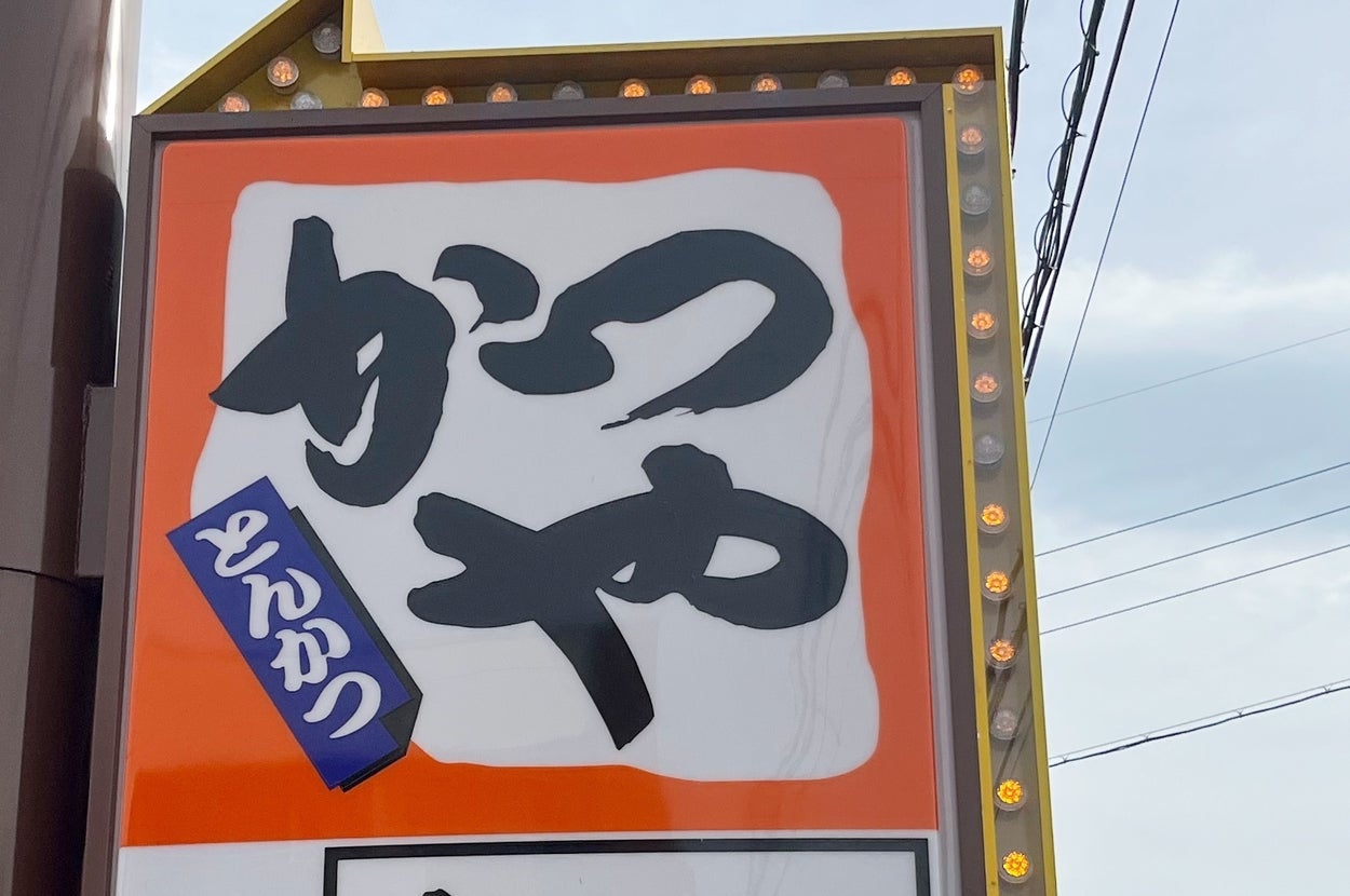 店の外にある「かつや」看板と矢印。とんかつやかつ弁当を提供する飲食店の案内。