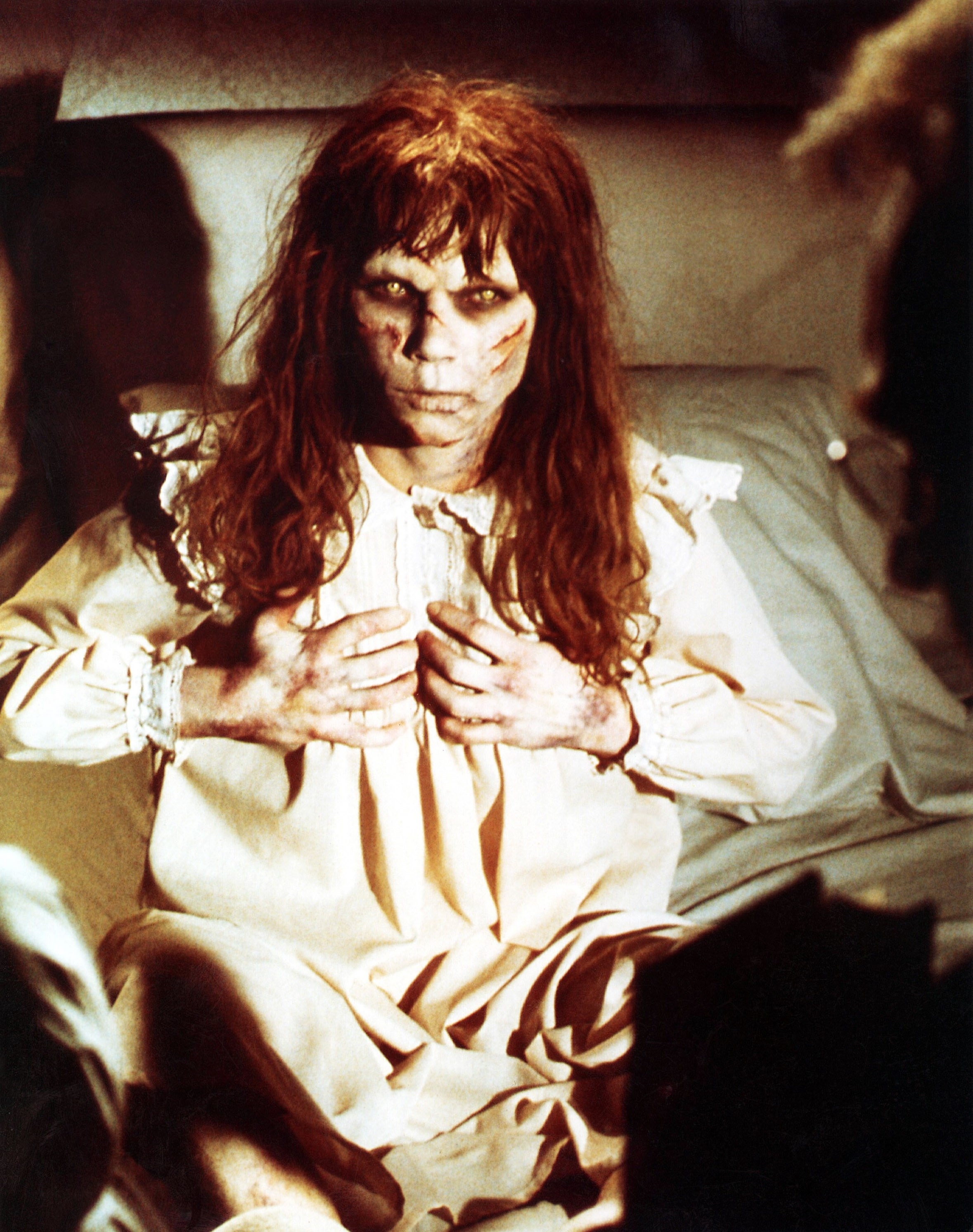 A character from &quot;The Exorcist&quot; sits on a bed with disheveled hair and a worn nightgown, portraying a possessed appearance