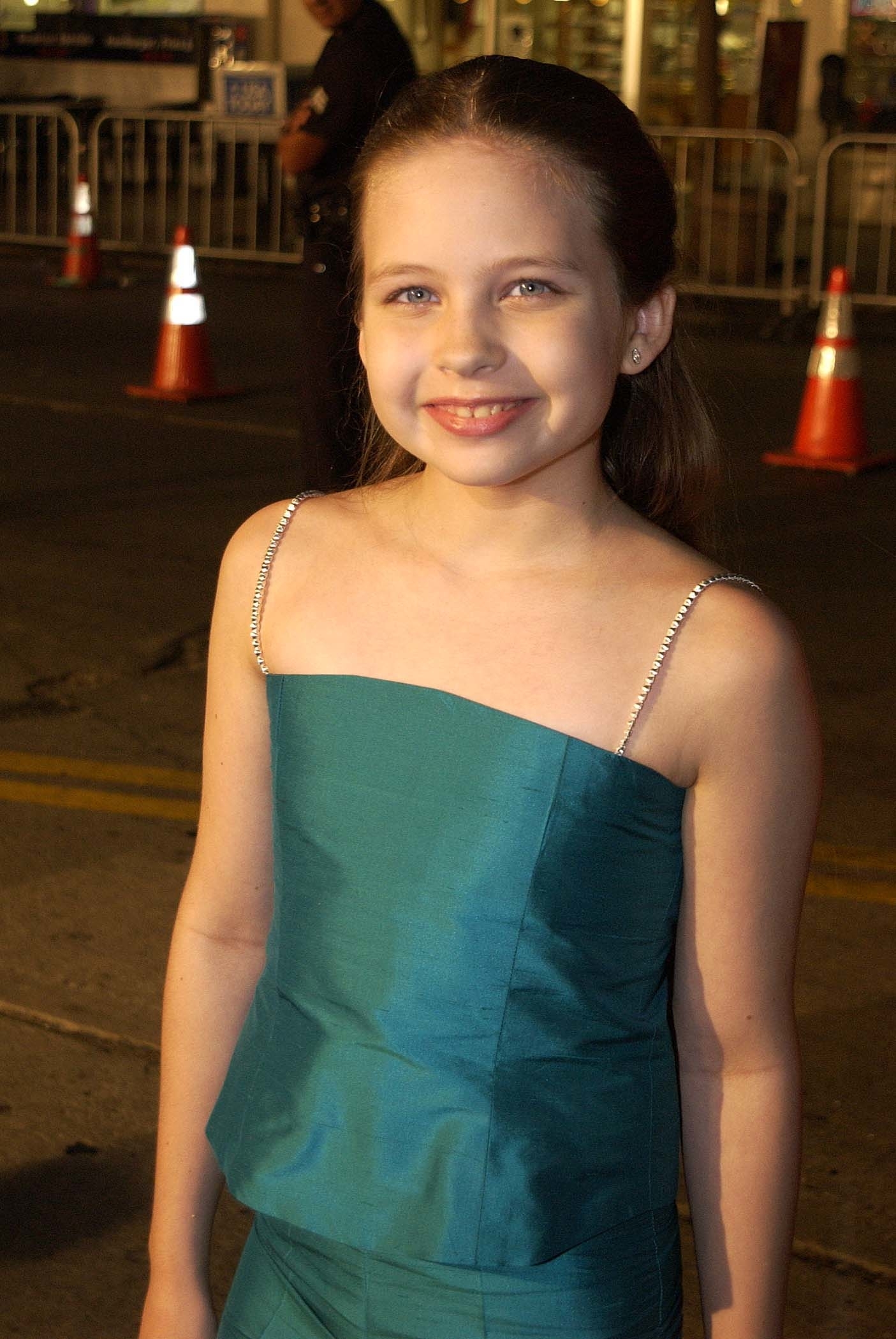 A young girl in a stylish evening dress smiles at a camera at an event