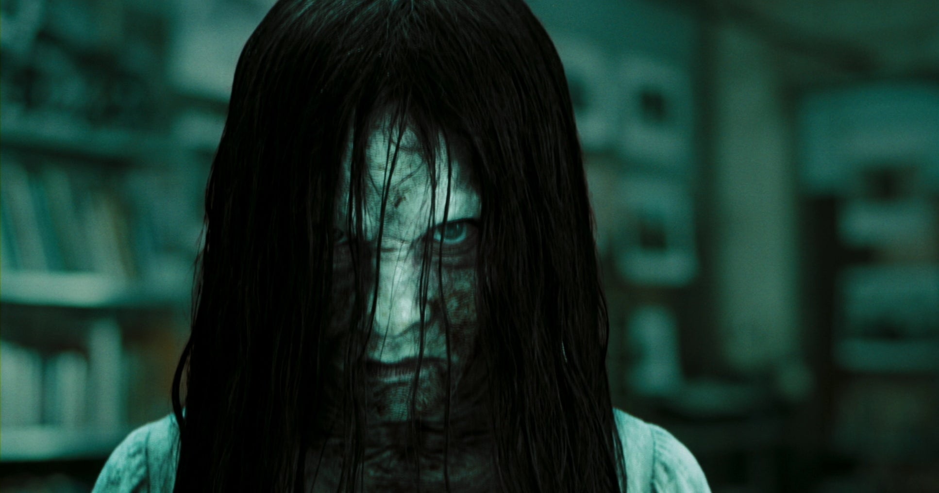 A creepy character with long dark hair and a pale, unsettling face stares directly at the viewer, suggesting a scene from a horror film