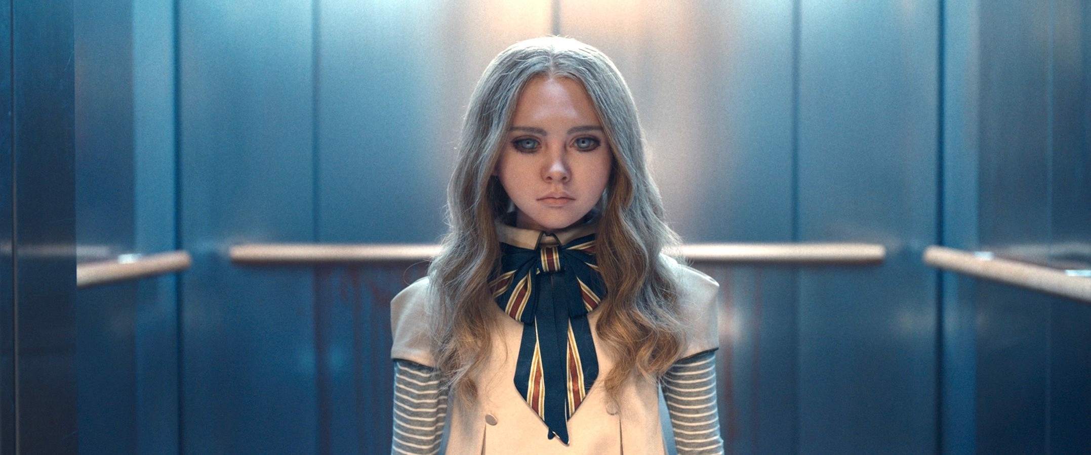 A character from TV or movie standing in an elevator, wearing a uniform with a striped bow and metallic sleeves. Identifying details are unavailable