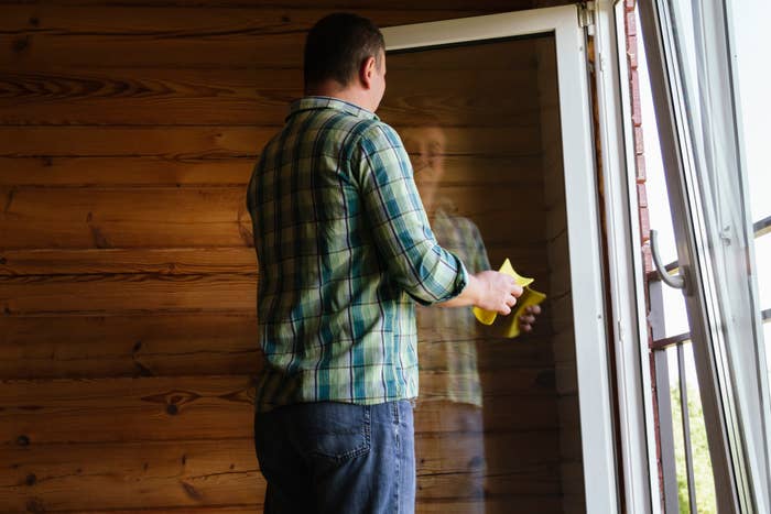Man cleaning a glass door with a cloth on a wooden cabin porch