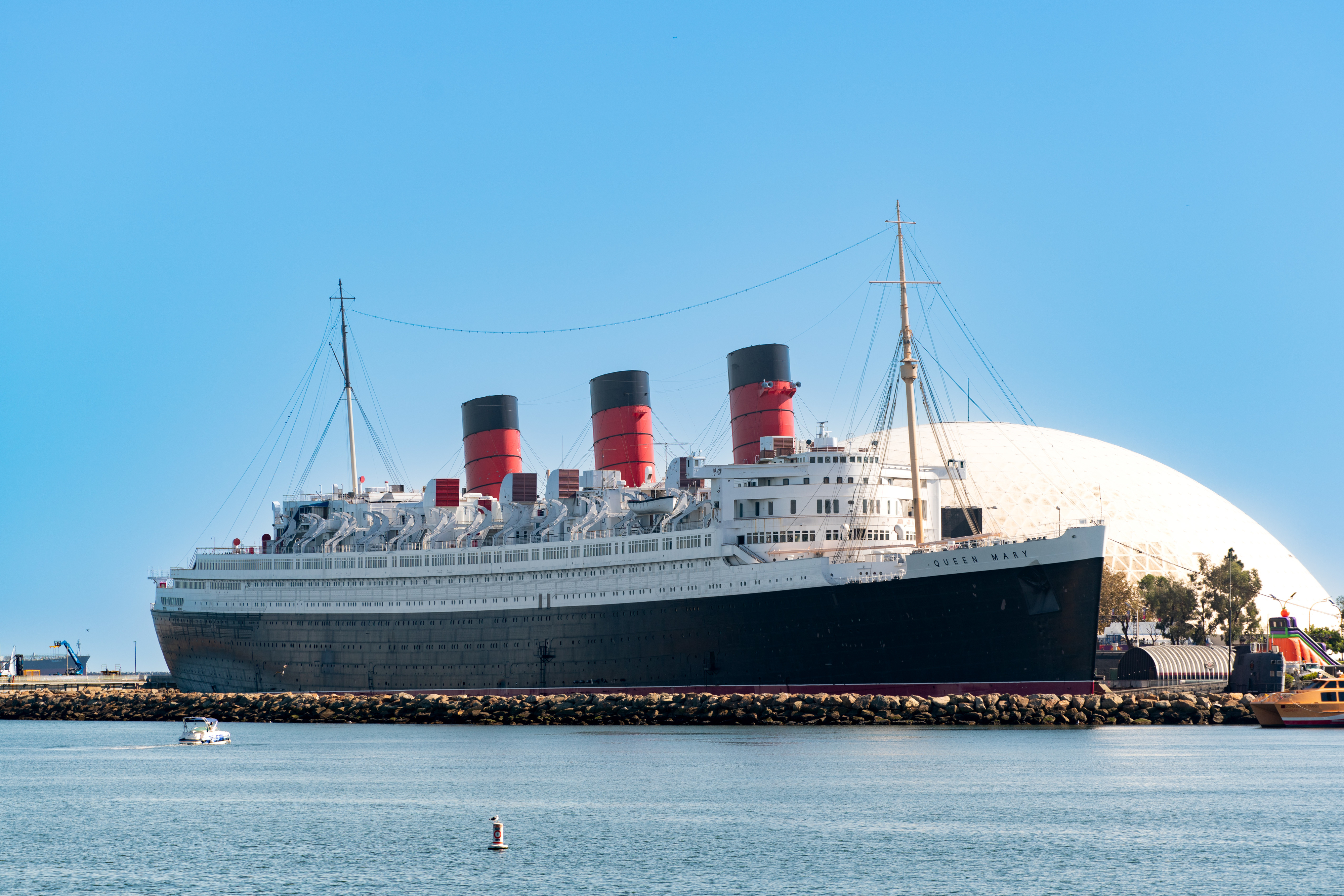 Historic ocean liner Queen Mary docked at a port, with a clear sky in the background