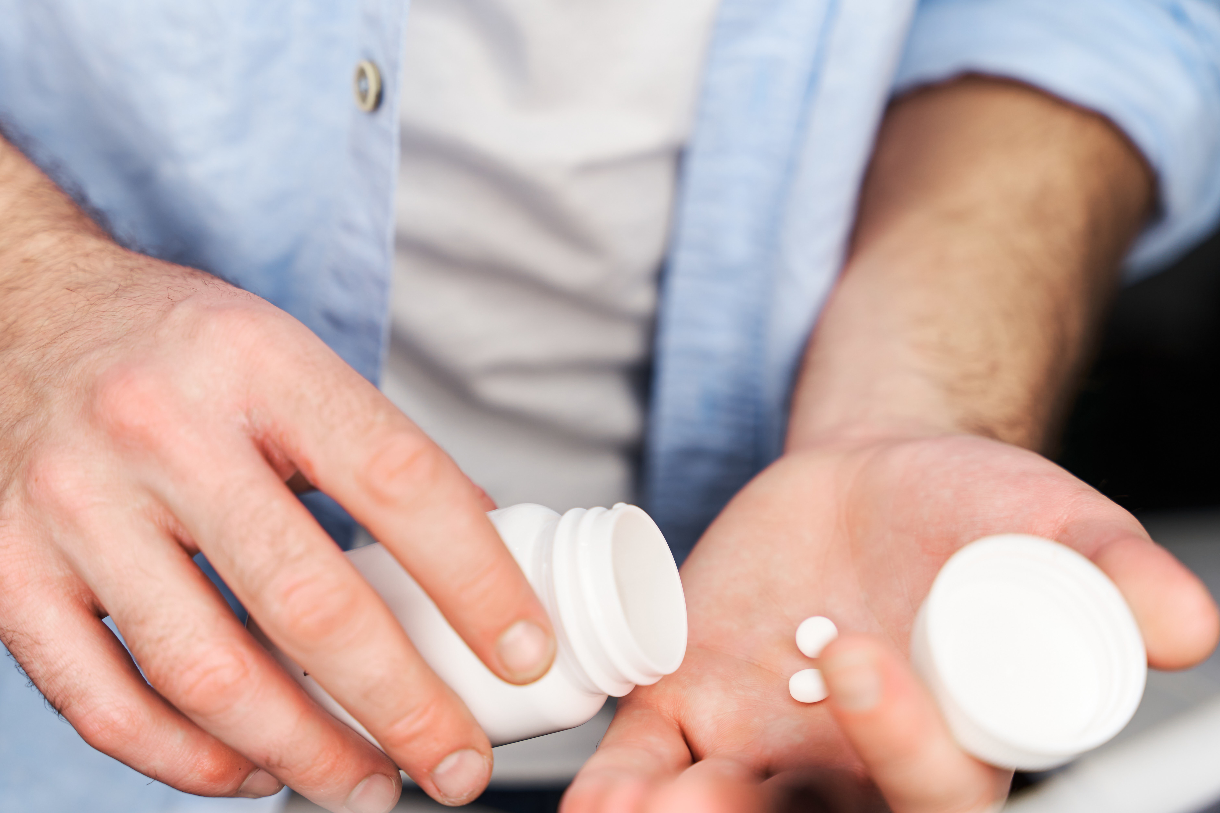 Person holding an open pill bottle, pouring two tablets into their hand, with a close-up of their hands and part of their shirt visible