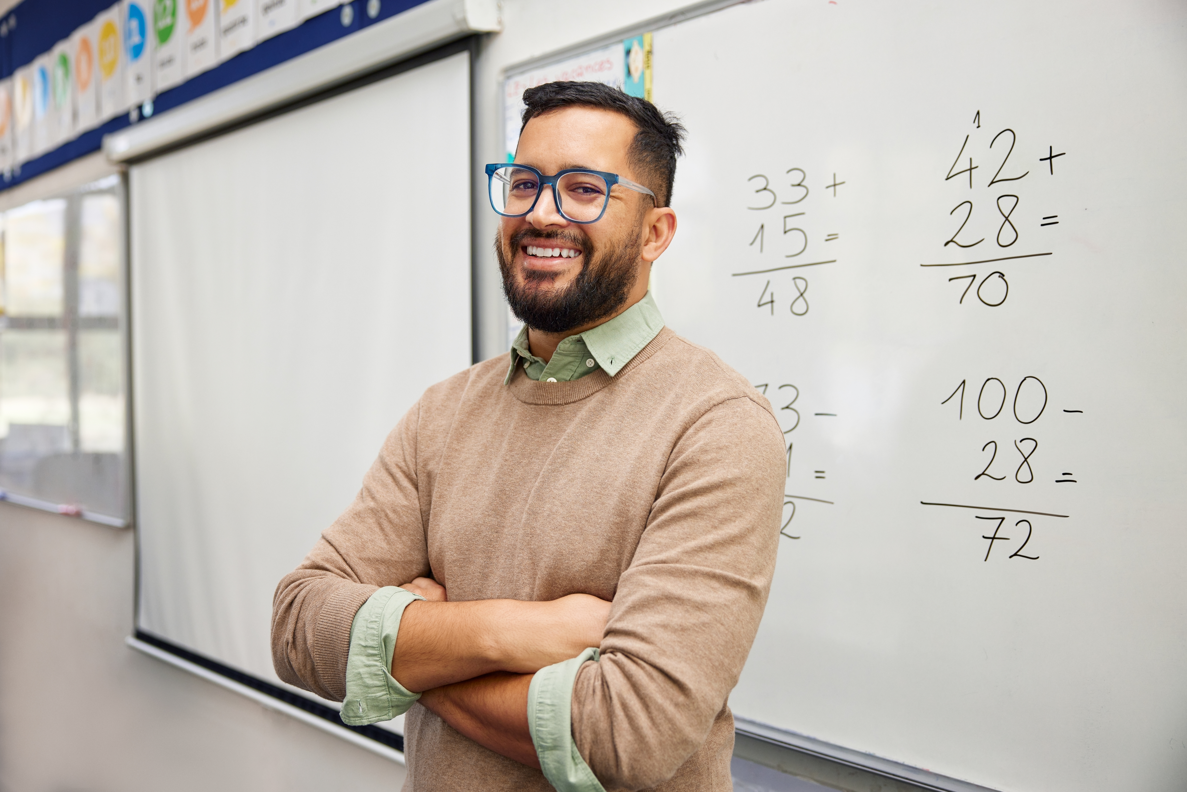 A person stands smiling in front of a whiteboard with math equations at a classroom