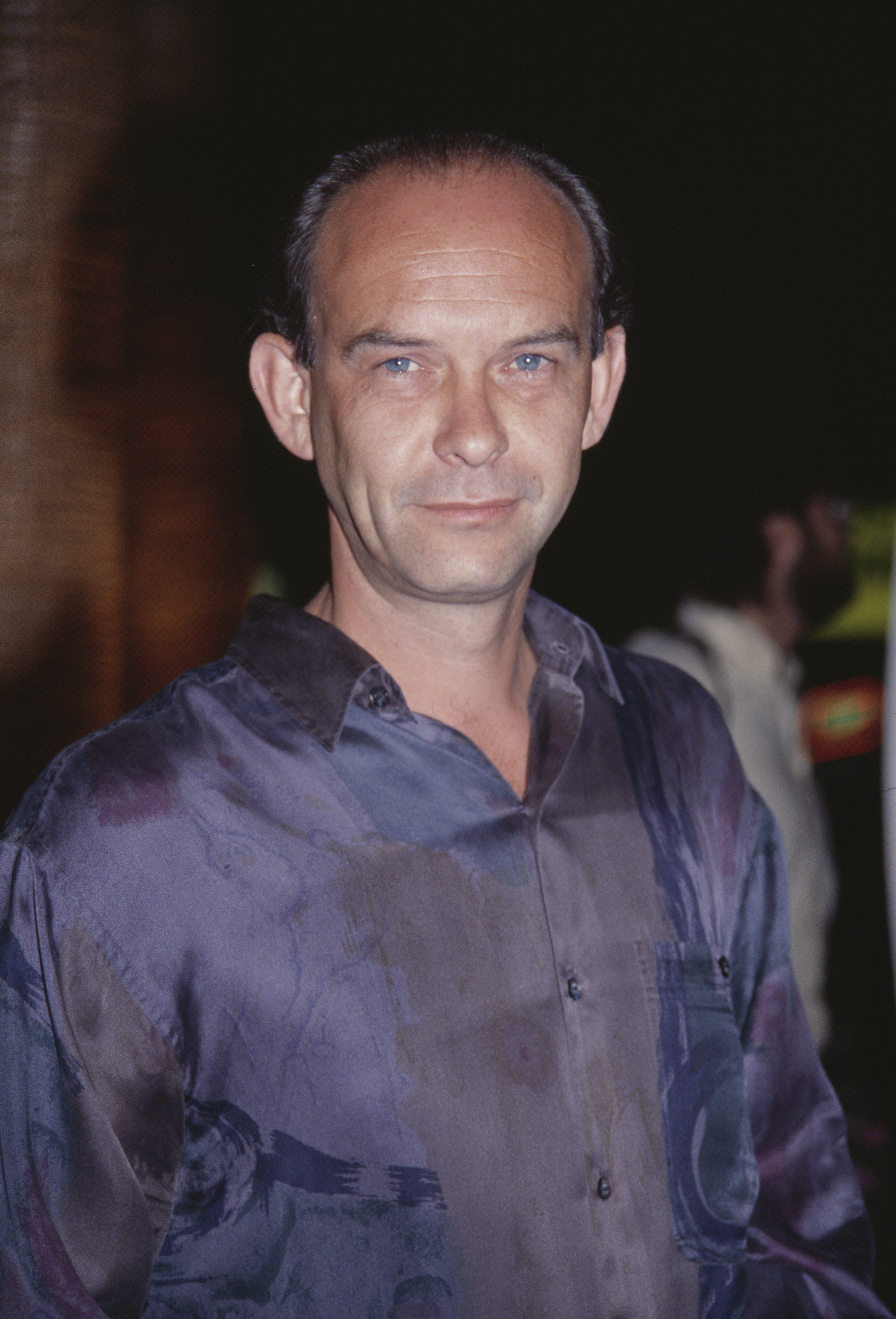 A man wearing a patterned button-up shirt on a red carpet