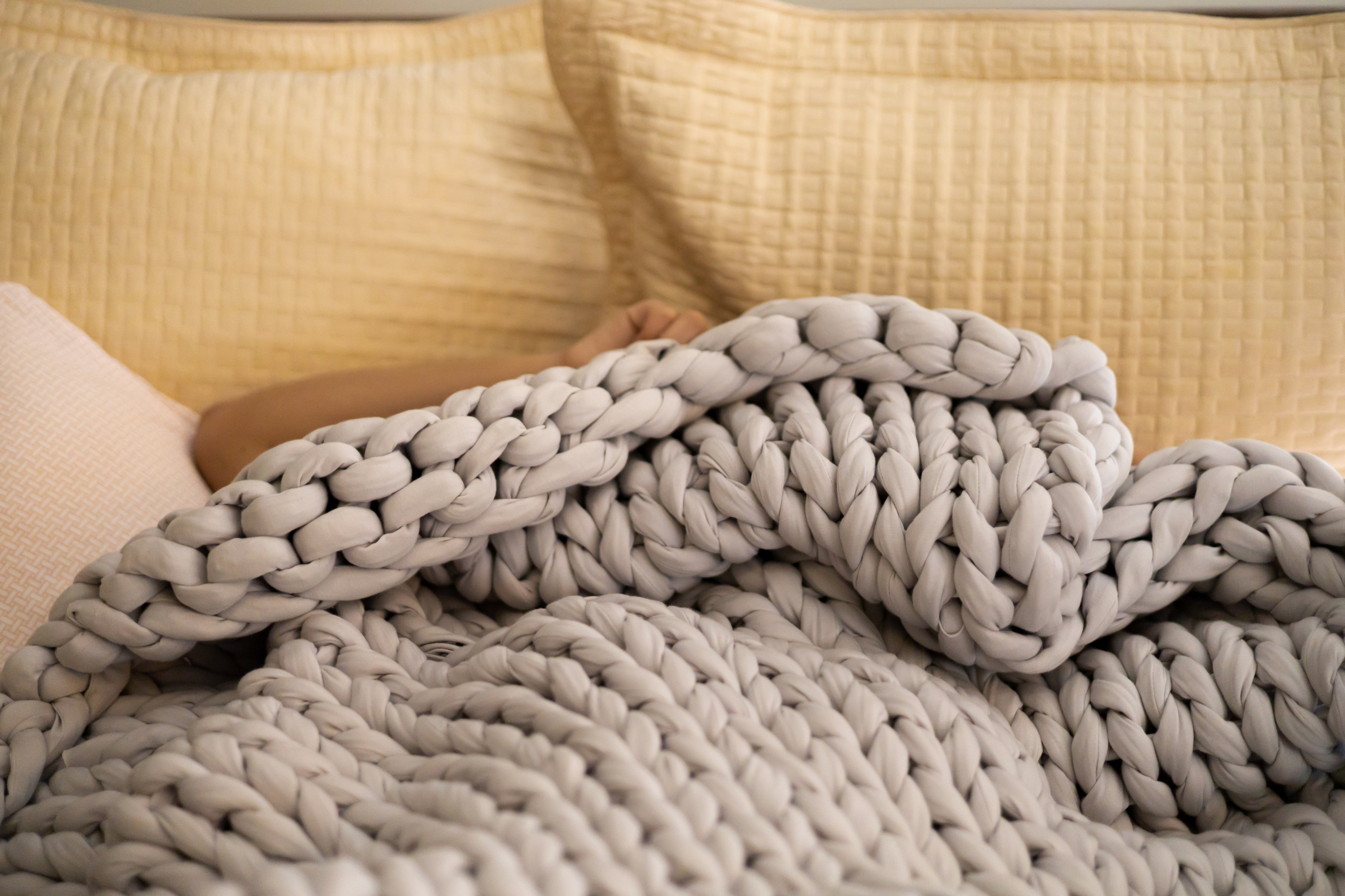 Person sleeping under a chunky knit blanket on a bed with quilted pillows