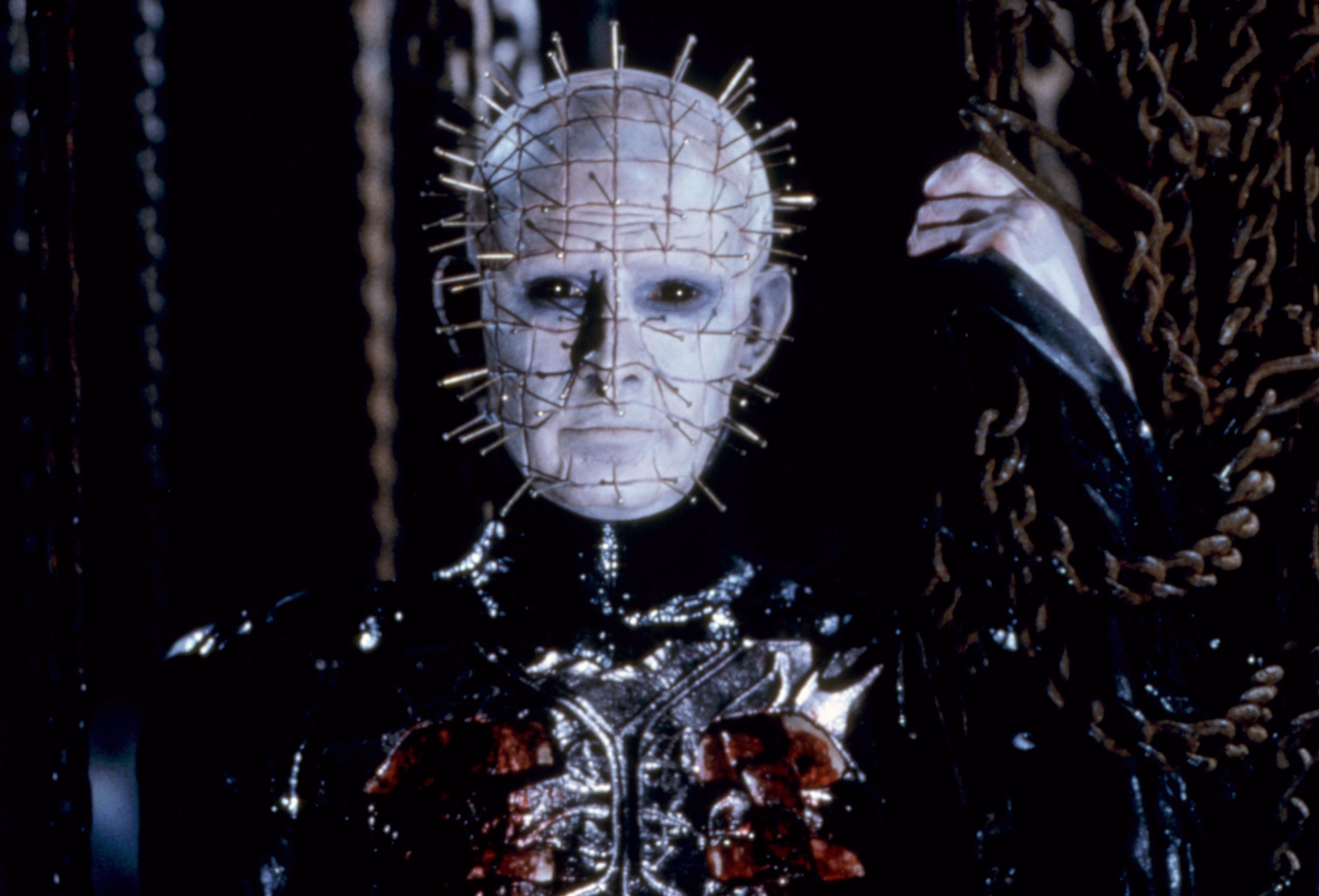 A character with pins in their head and a black leather outfit stands surrounded by chains