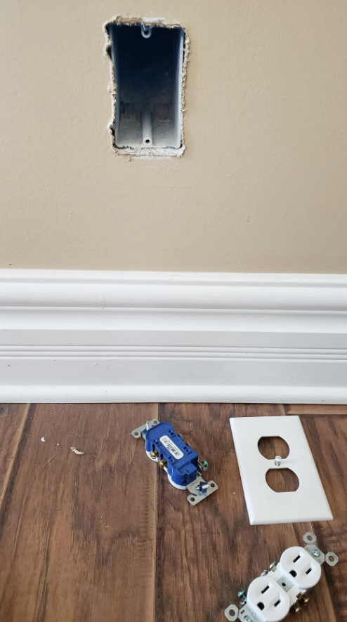 Electrical outlet installation in progress on a wall, with a blue outlet and faceplate on the floor