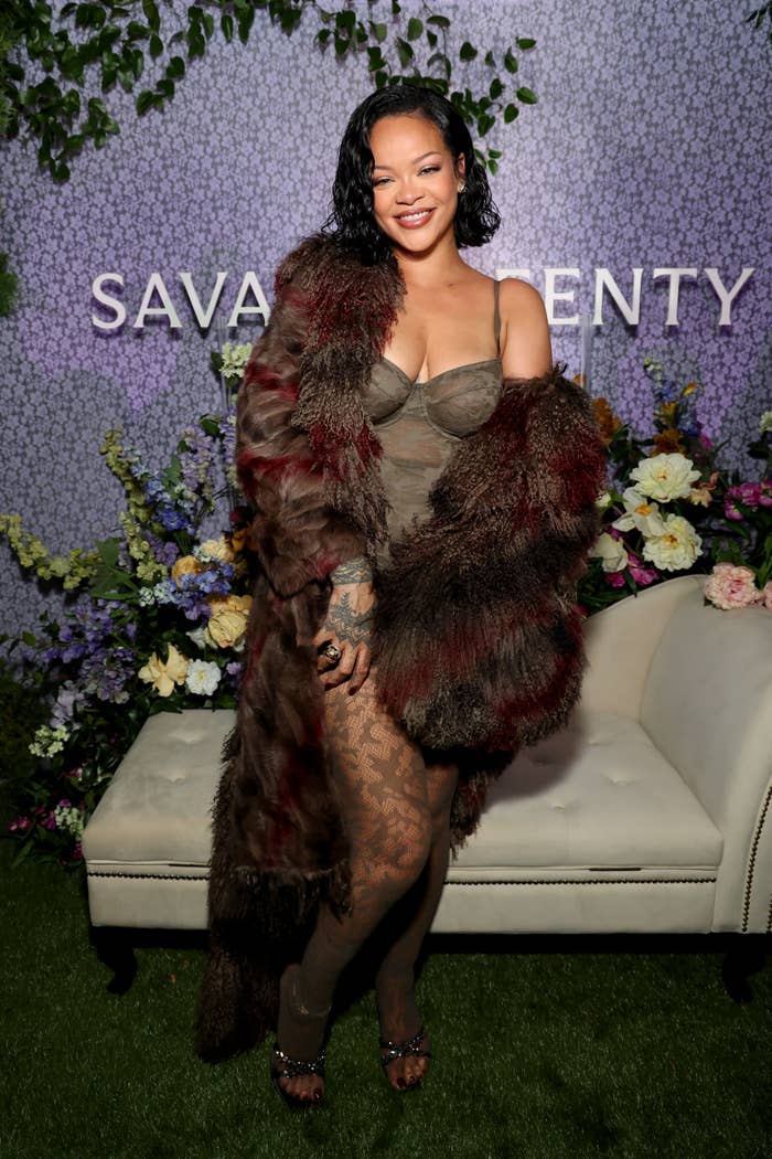 A person poses with a smile in stylish fur-trimmed attire at a Savage x Fenty event