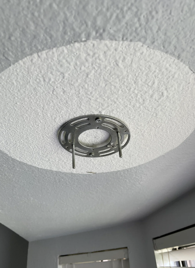 Ceiling view of a textured circular light fixture base, missing a light fixture. Room corners visible in the background