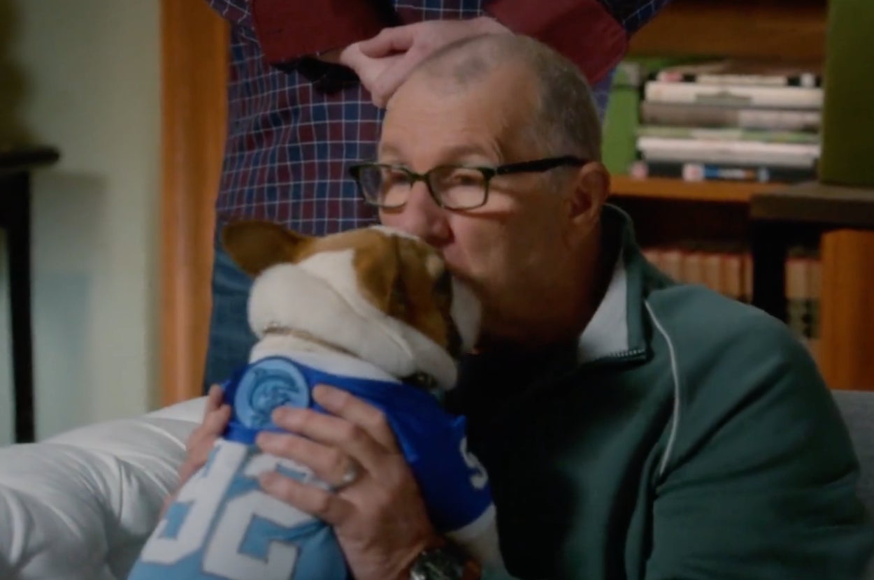 Man kissing a dog wearing jersey; books in background