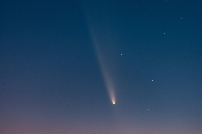 夜空に彗星が輝き、地平線の上に都市の明かりが見える景色。