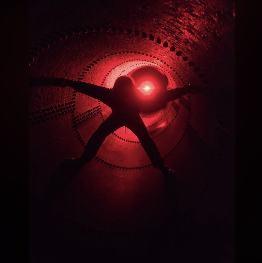 Silhouette of a person with arms and legs spread out inside a large tube with a red glowing light at the end