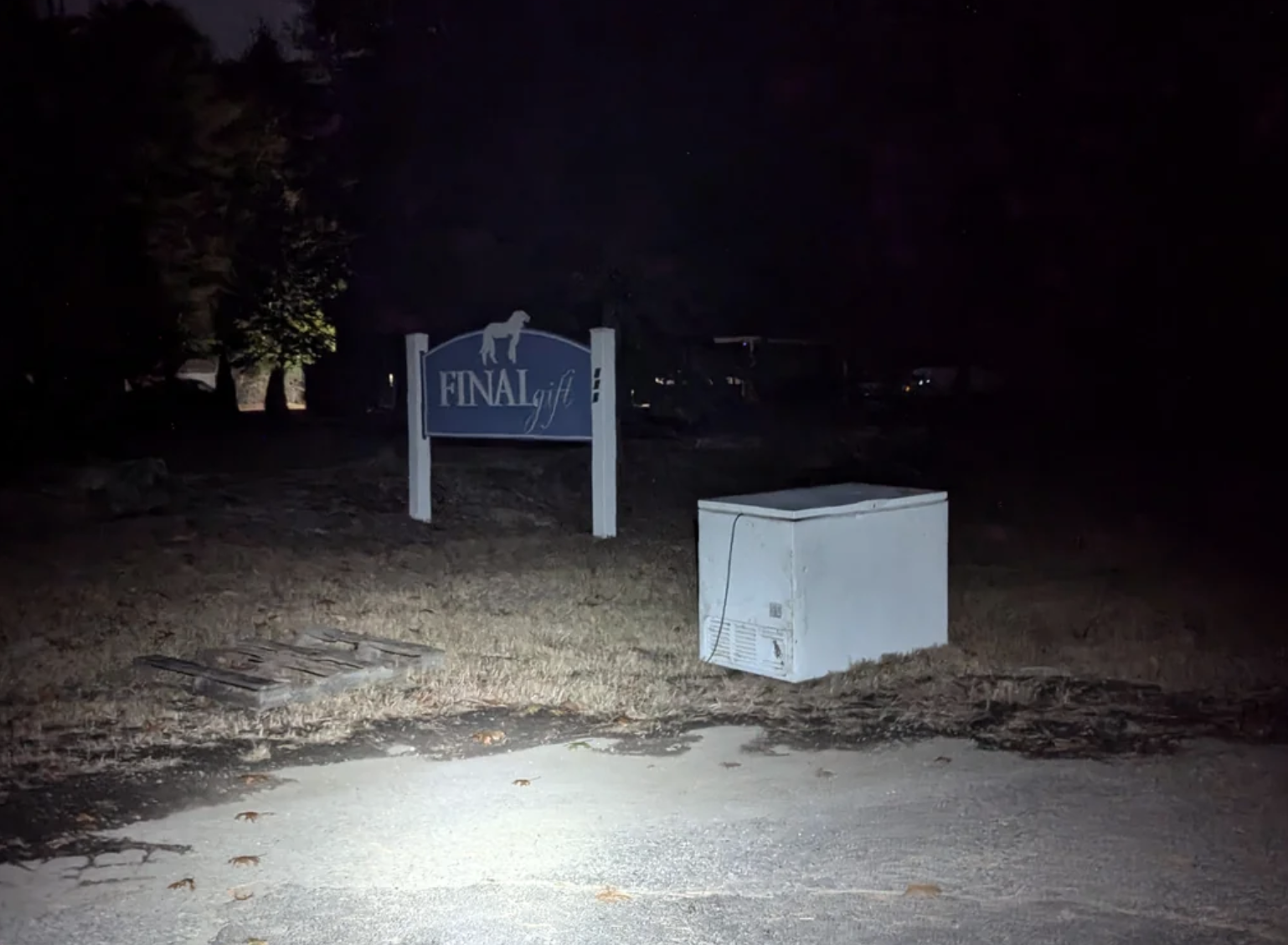 A dimly lit sign reads &quot;Final Gift&quot; with a small illuminated white box nearby, positioned on a sparsely vegetated ground