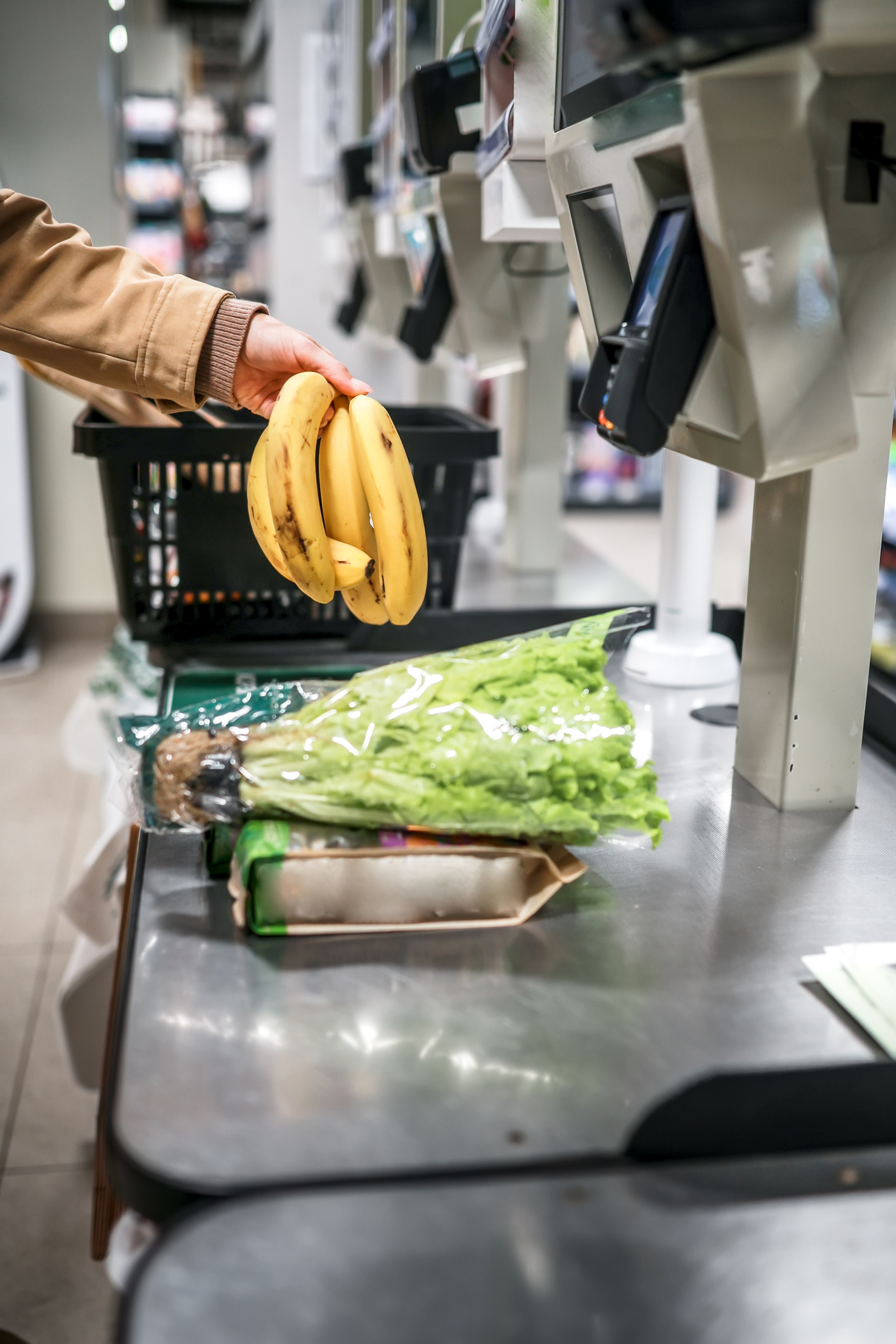 A person scans bananas, lettuce, and other groceries at a self-checkout in a store