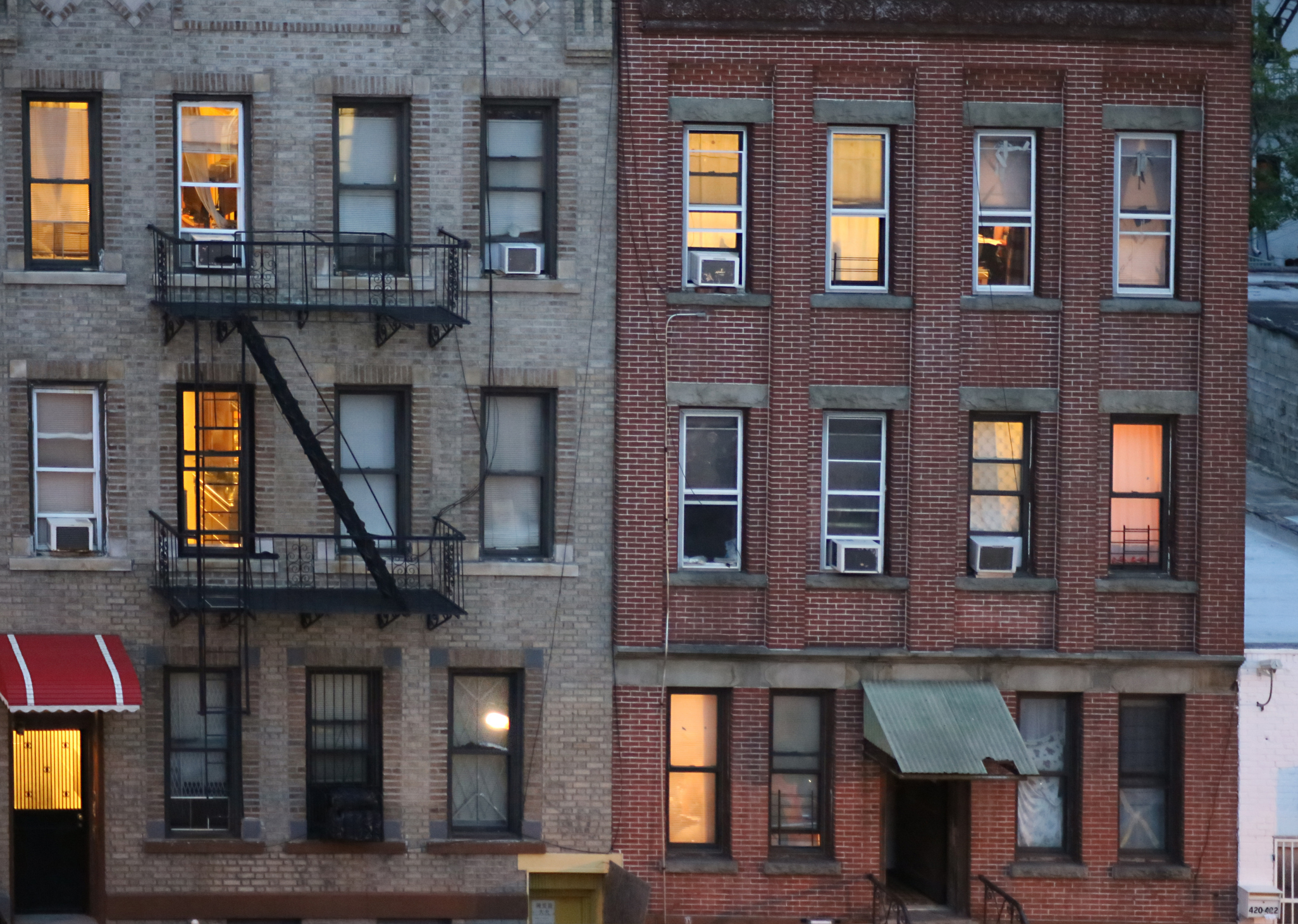 Two adjacent brick apartment buildings with lit windows and fire escapes