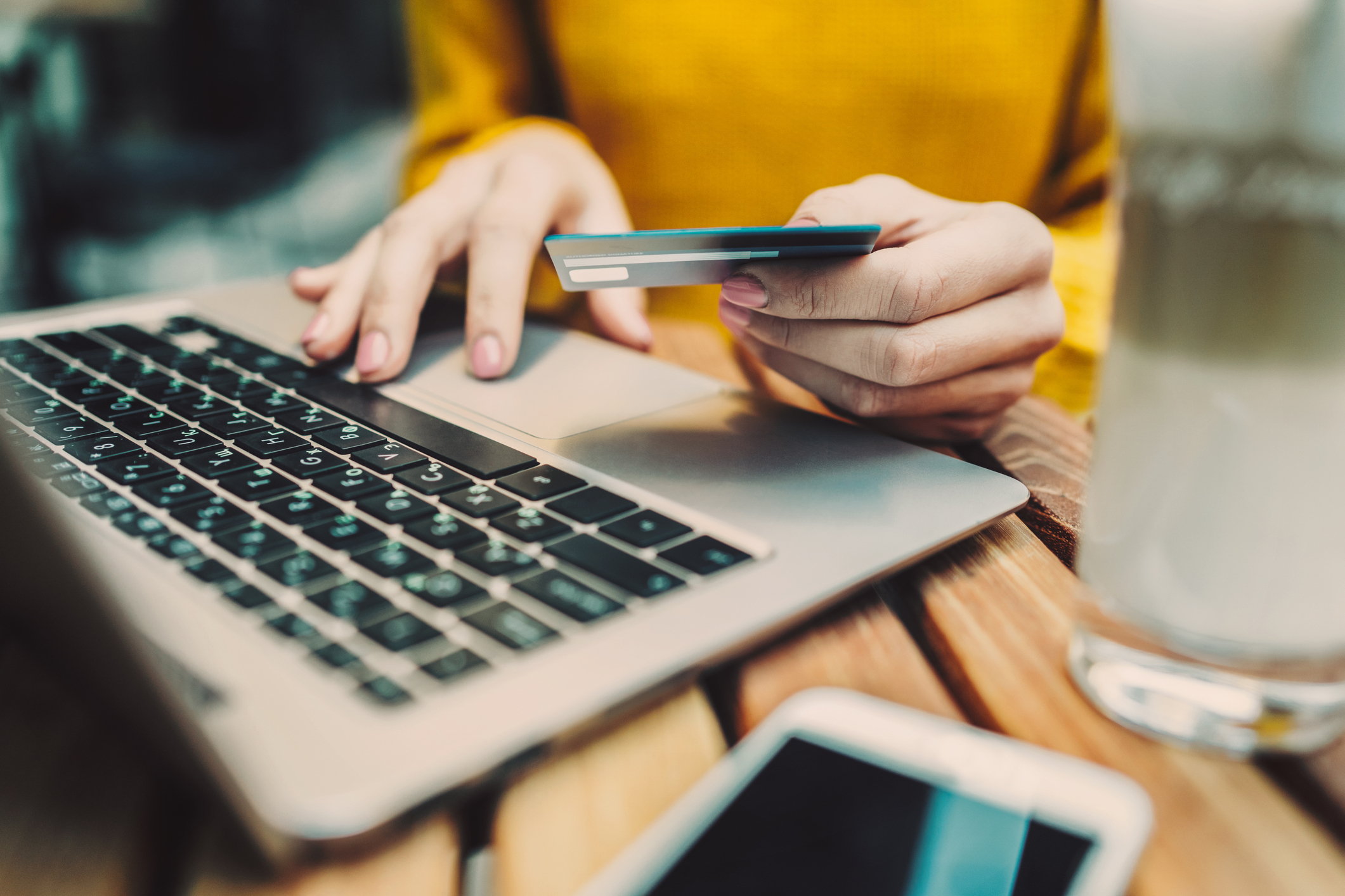 Person using a laptop, holding a credit card, with a smartphone nearby