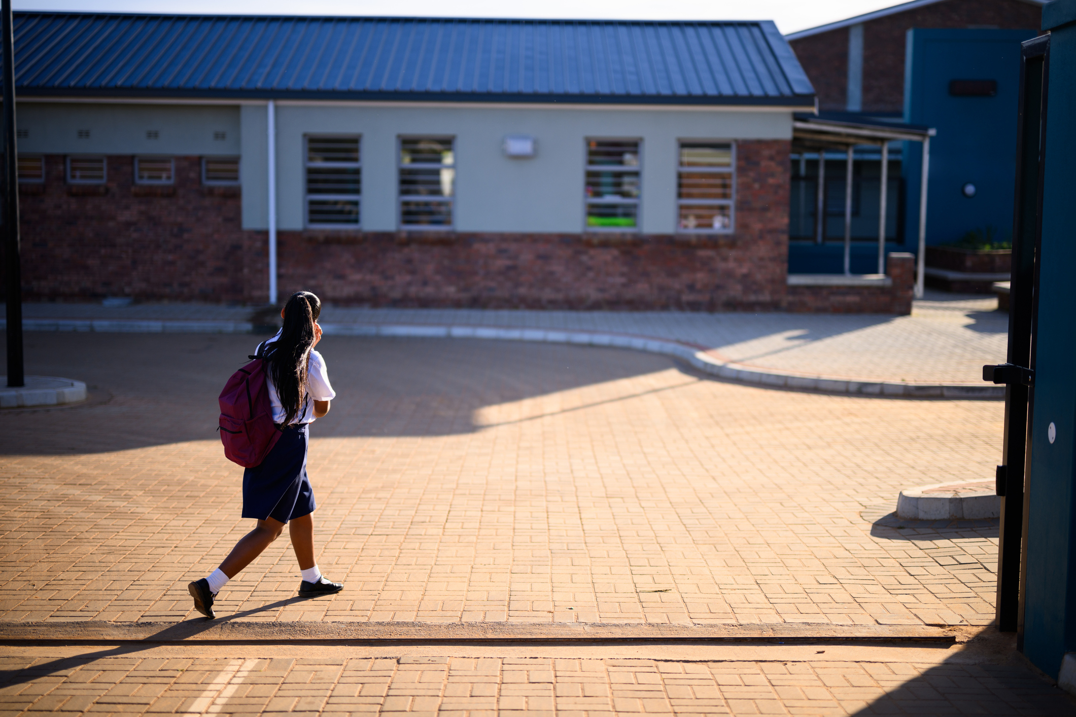 Student with a backpack walks alone past a brick school building