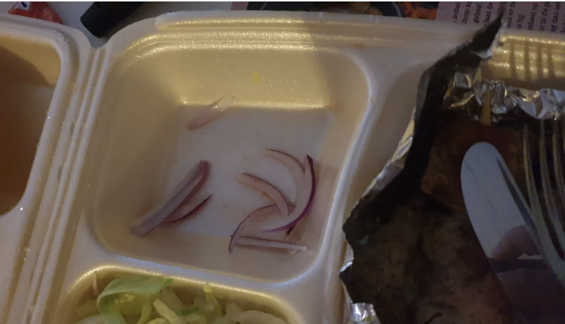 A few slices of red onion in a food container with foil-covered contents and lettuce