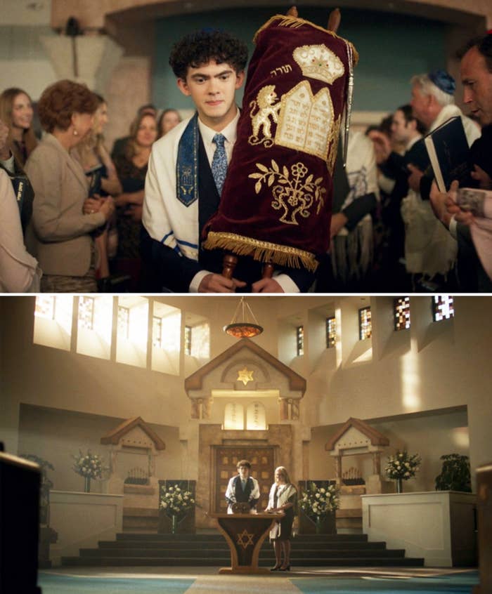 Billy stands in a synagogue holding a Torah, surrounded by people, and later speaks at a podium with a Star of David in a beautifully-lit space