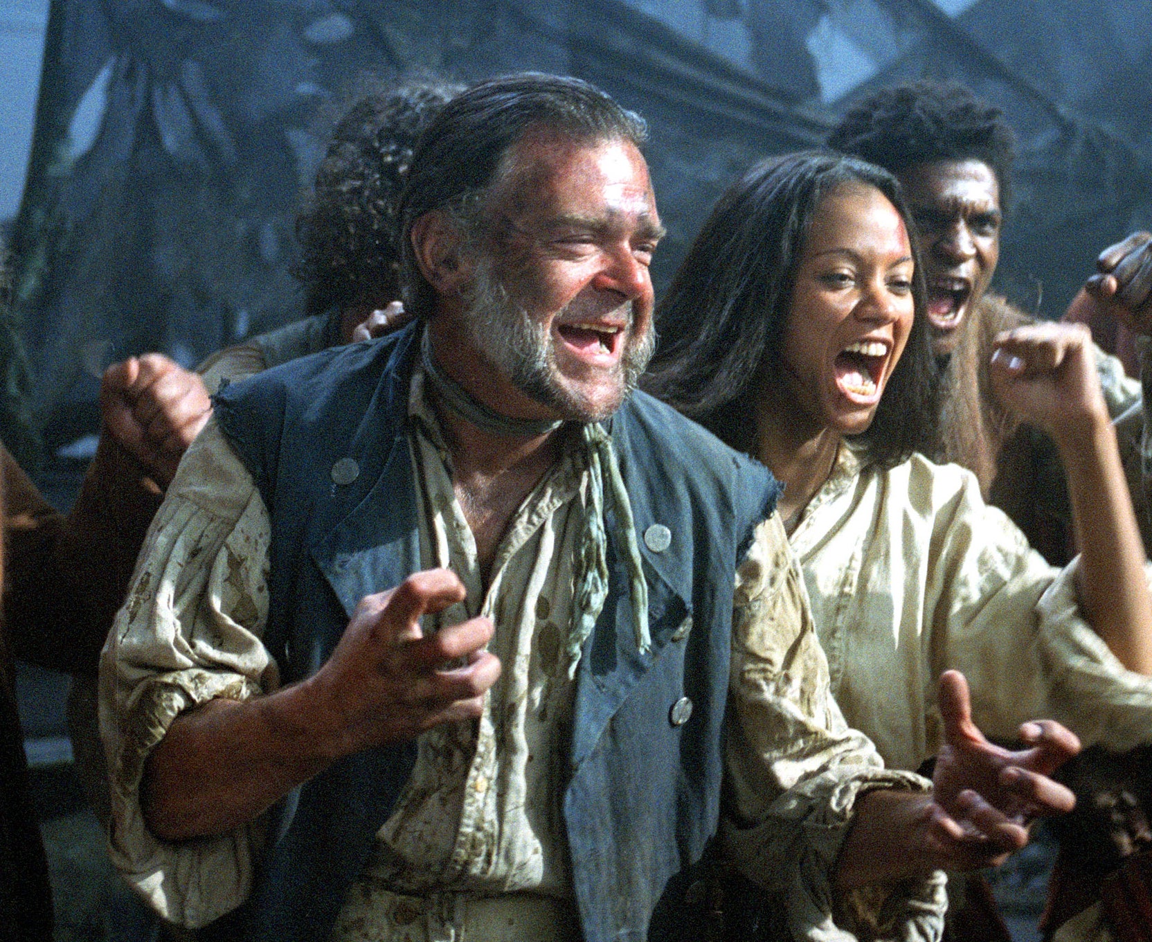 Group of actors in pirate costumes, cheering with fists raised, in a movie scene with tattered sails in the background