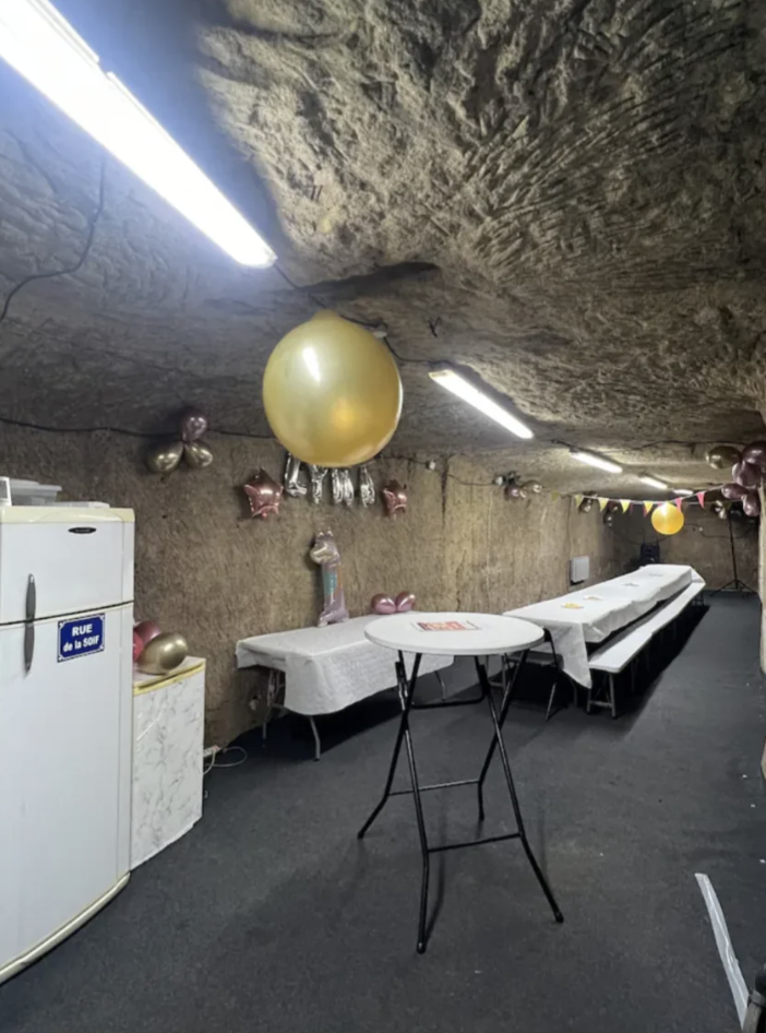 Underground cave decorated for a party with tables, a fridge, balloons, and hanging lights